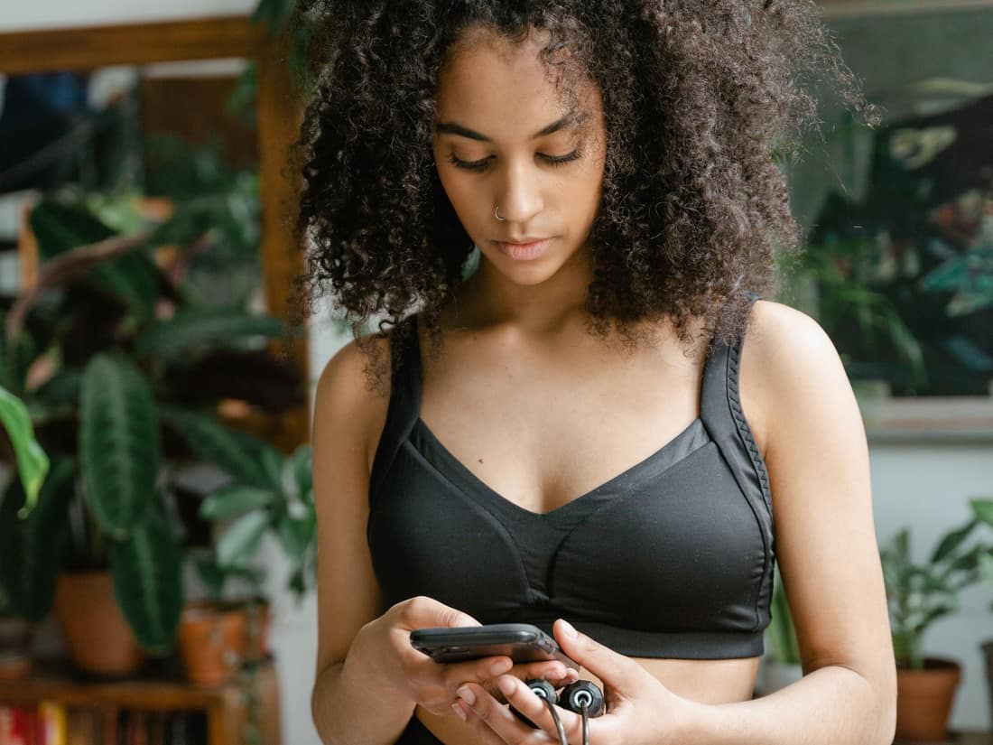 Woman in workout clothes following her plan on her phone at home